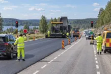 Illustrationsbild av vägarbetare som dirigerar trafik förbi en asfalteringsmaskin