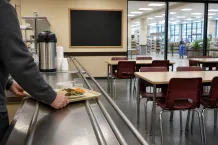 Man skjuter en bricka med husmanskost längs en självserveringsdisk i en ljus lunchmatsal.